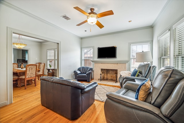 living room with a fireplace, light hardwood / wood-style floors, ceiling fan, and crown molding