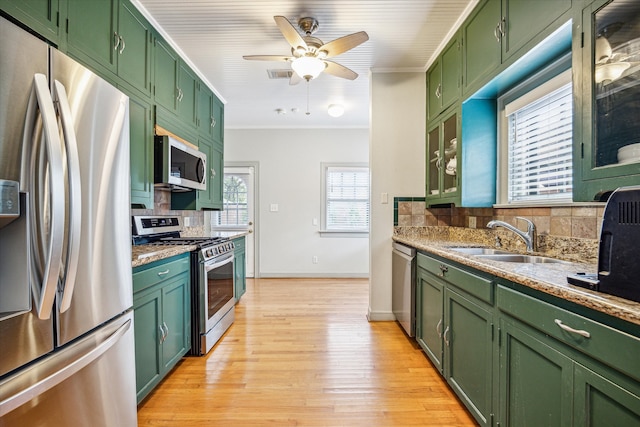 kitchen featuring tasteful backsplash, light stone counters, appliances with stainless steel finishes, green cabinetry, and light hardwood / wood-style flooring