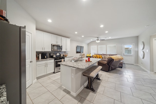 kitchen with white cabinetry, appliances with stainless steel finishes, light stone countertops, backsplash, and an island with sink