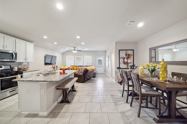 kitchen with stainless steel appliances, white cabinetry, light stone countertops, sink, and a breakfast bar area