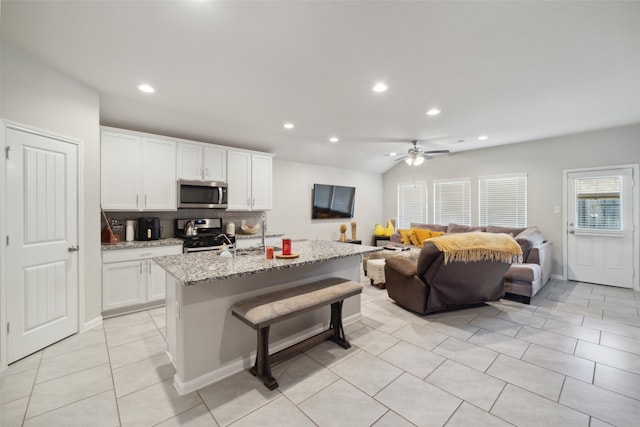 kitchen with light stone counters, tasteful backsplash, a kitchen island with sink, white cabinetry, and appliances with stainless steel finishes