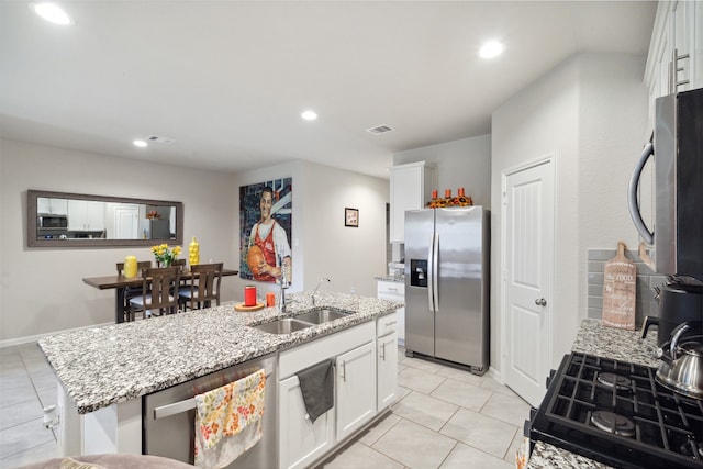 kitchen with stainless steel appliances, light stone countertops, white cabinets, and an island with sink