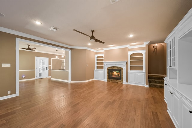 unfurnished living room featuring a stone fireplace, ornamental molding, and hardwood / wood-style flooring