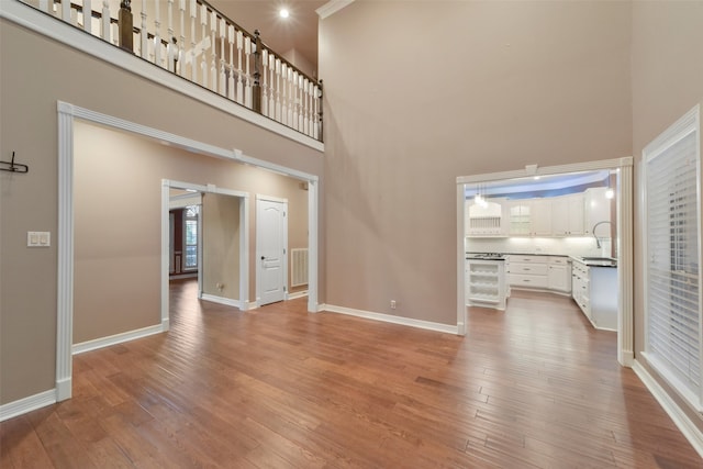 unfurnished living room featuring a towering ceiling, wine cooler, light wood-type flooring, and sink