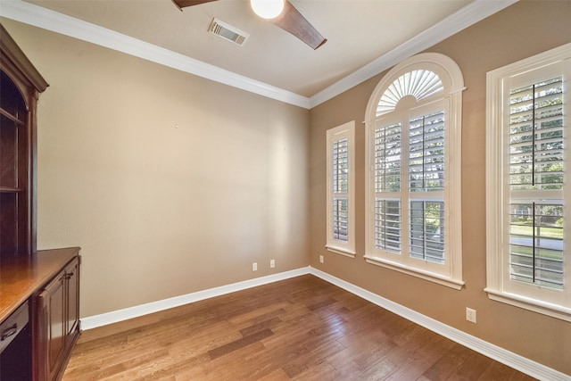 empty room with ornamental molding, ceiling fan, a wealth of natural light, and light hardwood / wood-style floors