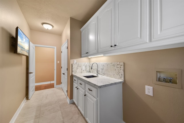 clothes washing area featuring light tile patterned flooring, washer hookup, a textured ceiling, cabinets, and sink