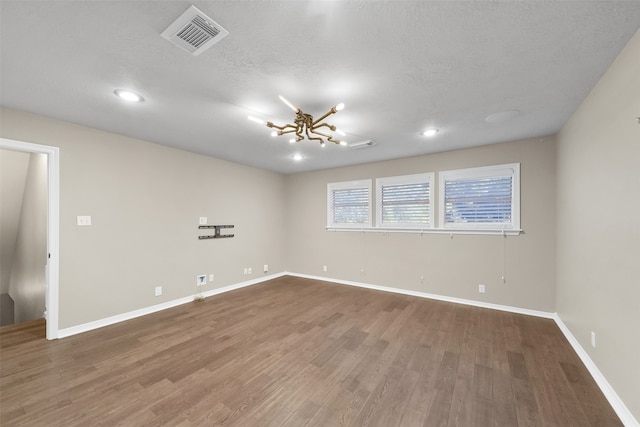 spare room with hardwood / wood-style floors, a chandelier, and a textured ceiling