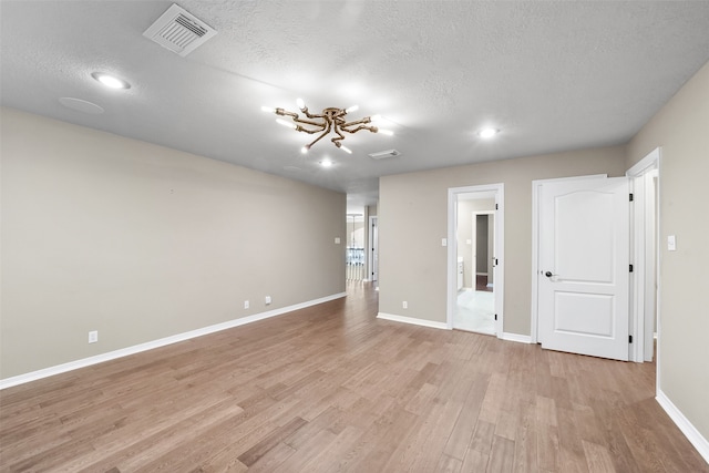 spare room with a textured ceiling, light hardwood / wood-style flooring, and a notable chandelier