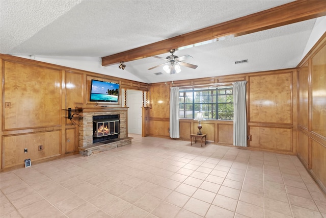 unfurnished living room featuring a stone fireplace, wood walls, ceiling fan, and a textured ceiling