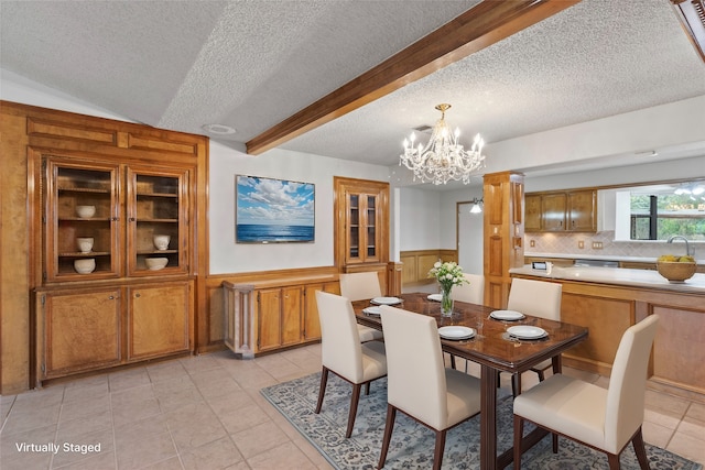 tiled dining space with wood walls, a notable chandelier, lofted ceiling with beams, and a textured ceiling