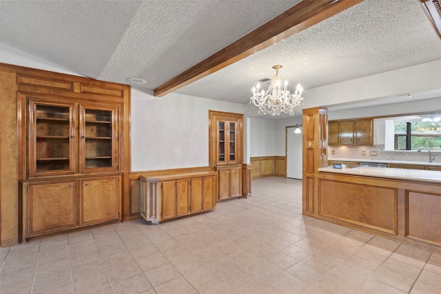 kitchen featuring pendant lighting, backsplash, wooden walls, a textured ceiling, and a notable chandelier