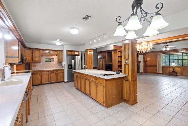 kitchen with backsplash, ceiling fan with notable chandelier, sink, stainless steel fridge, and decorative light fixtures