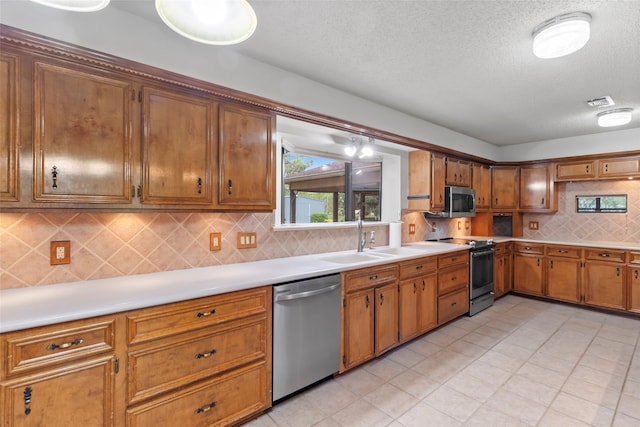 kitchen with tasteful backsplash, a textured ceiling, stainless steel appliances, sink, and light tile patterned floors