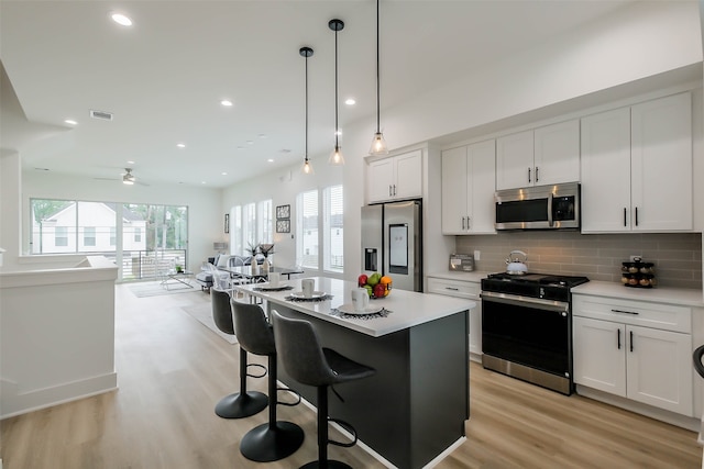 kitchen featuring appliances with stainless steel finishes, ceiling fan, white cabinets, a kitchen island, and hanging light fixtures