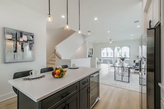 kitchen with a kitchen island, light hardwood / wood-style flooring, white cabinets, wine cooler, and hanging light fixtures