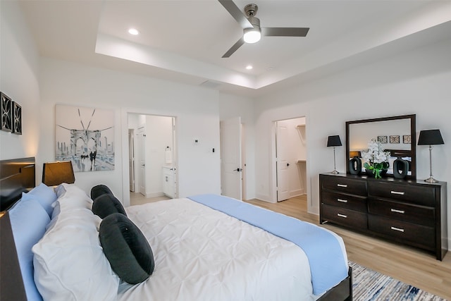 bedroom featuring ensuite bathroom, a raised ceiling, ceiling fan, and light hardwood / wood-style flooring