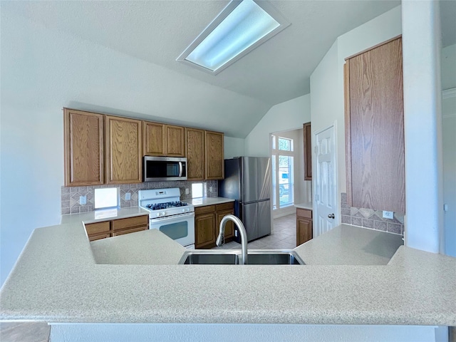 kitchen featuring lofted ceiling, stainless steel appliances, a sink, decorative backsplash, and brown cabinets