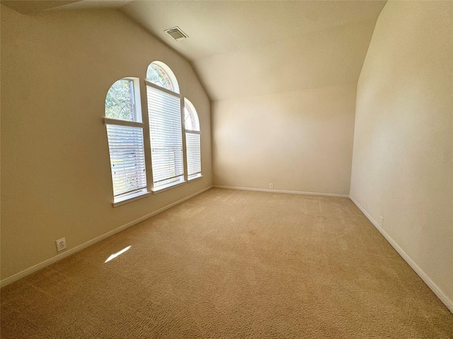 unfurnished room with vaulted ceiling, light carpet, visible vents, and baseboards