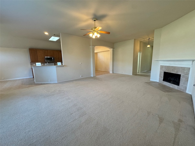 unfurnished living room with arched walkways, light carpet, a fireplace, a ceiling fan, and baseboards