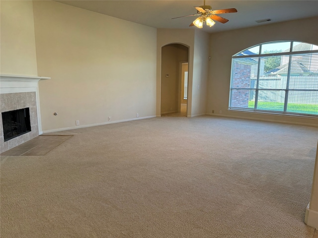 unfurnished living room with light carpet, visible vents, arched walkways, a ceiling fan, and a tile fireplace