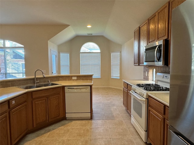 kitchen featuring appliances with stainless steel finishes, vaulted ceiling, brown cabinetry, and a sink