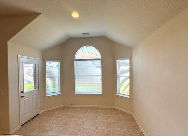 tiled spare room featuring a textured ceiling and lofted ceiling