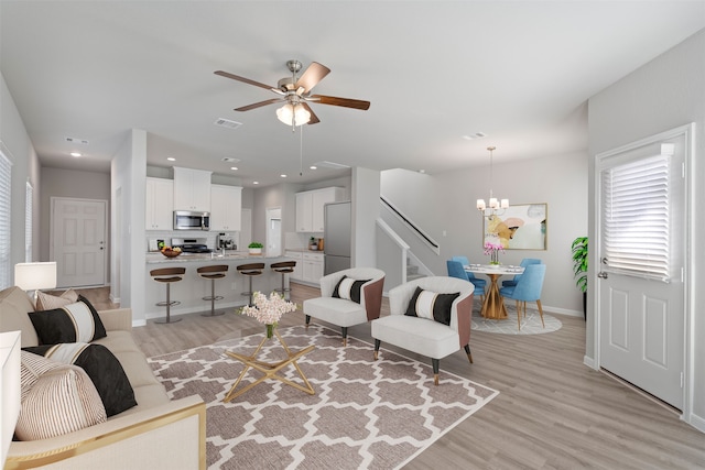 living room with ceiling fan with notable chandelier and light hardwood / wood-style flooring