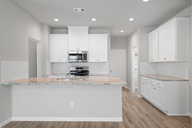 kitchen featuring white cabinets, light stone countertops, appliances with stainless steel finishes, and light hardwood / wood-style flooring