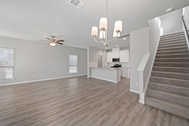 unfurnished living room featuring light hardwood / wood-style floors, ceiling fan with notable chandelier, and plenty of natural light