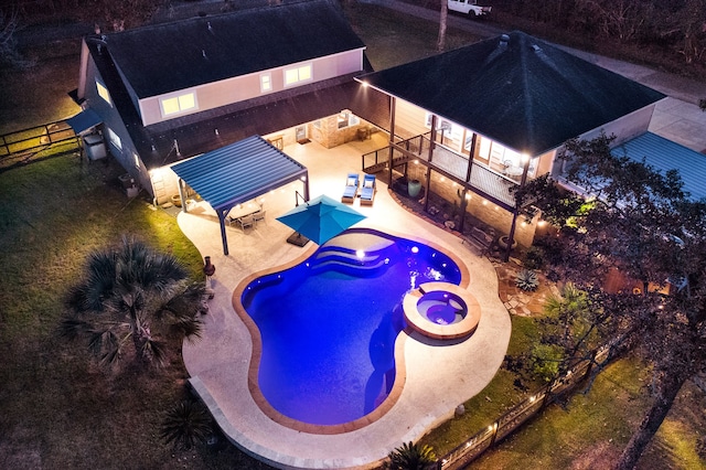 pool at night with a patio area and an in ground hot tub