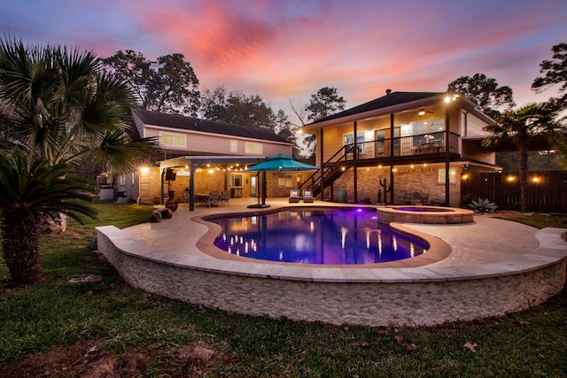 pool at dusk featuring an in ground hot tub and a patio