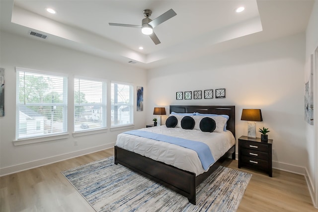 bedroom with light hardwood / wood-style floors, ceiling fan, and a tray ceiling