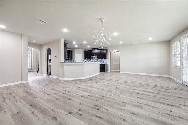 unfurnished living room with light wood-type flooring and a notable chandelier