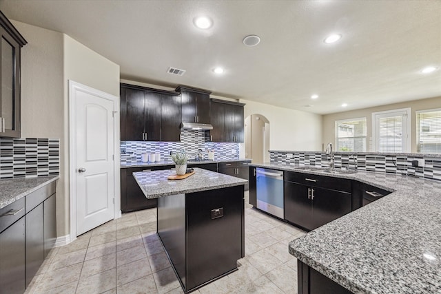 kitchen with light stone counters, backsplash, sink, dishwasher, and a center island