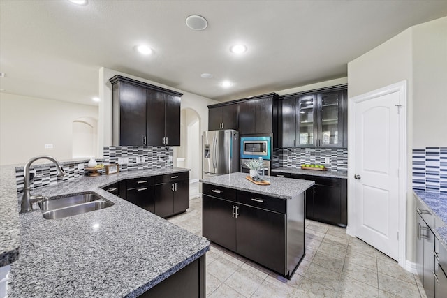 kitchen with a kitchen island, backsplash, appliances with stainless steel finishes, light stone countertops, and sink