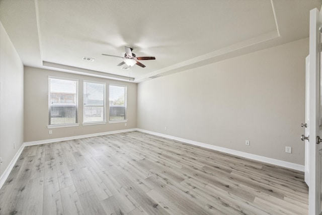 spare room with ceiling fan, a raised ceiling, and light wood-type flooring