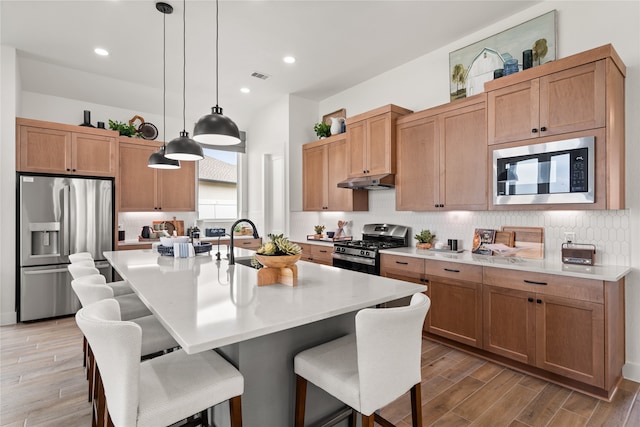 kitchen with a kitchen breakfast bar, backsplash, stainless steel appliances, hanging light fixtures, and an island with sink