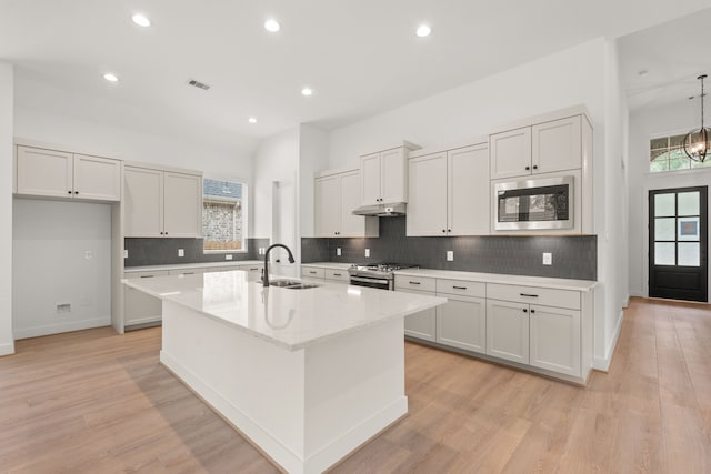 kitchen featuring sink, light wood-type flooring, stainless steel appliances, a kitchen island with sink, and white cabinets