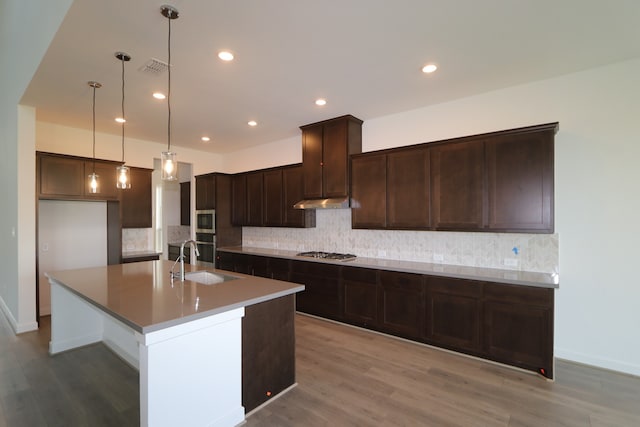 kitchen featuring stainless steel appliances, hanging light fixtures, hardwood / wood-style flooring, sink, and an island with sink