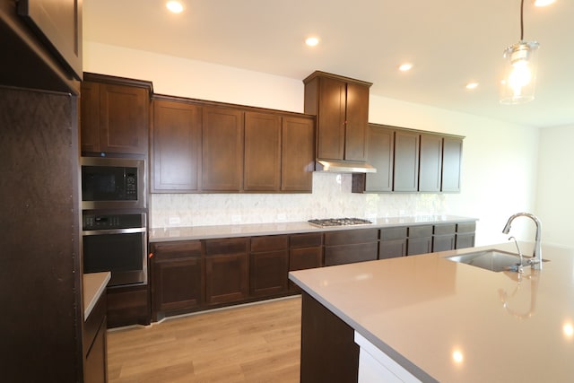 kitchen with hanging light fixtures, sink, tasteful backsplash, light wood-type flooring, and appliances with stainless steel finishes