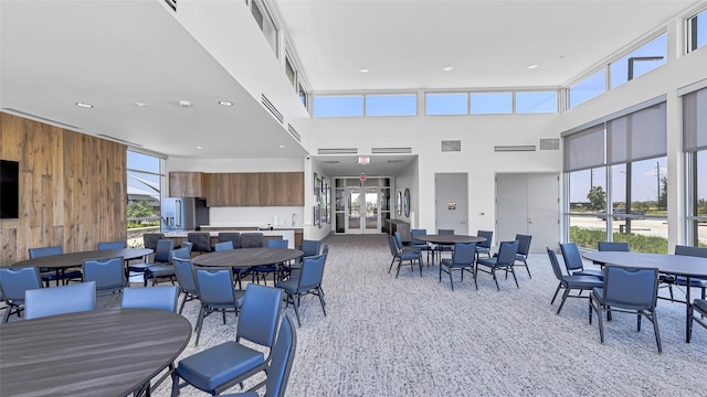 carpeted dining area featuring wood walls and a towering ceiling