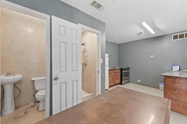 bathroom featuring tile patterned floors, toilet, tile walls, a textured ceiling, and a shower