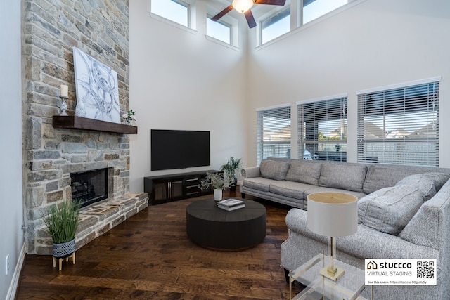 living room featuring ceiling fan, a stone fireplace, a towering ceiling, and a healthy amount of sunlight