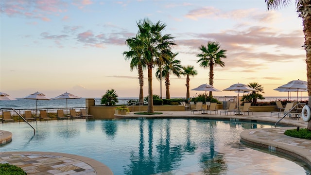 pool at dusk featuring a water view and a patio area