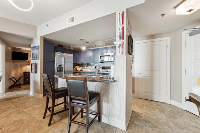 kitchen with a kitchen bar, backsplash, stainless steel appliances, sink, and dark stone countertops