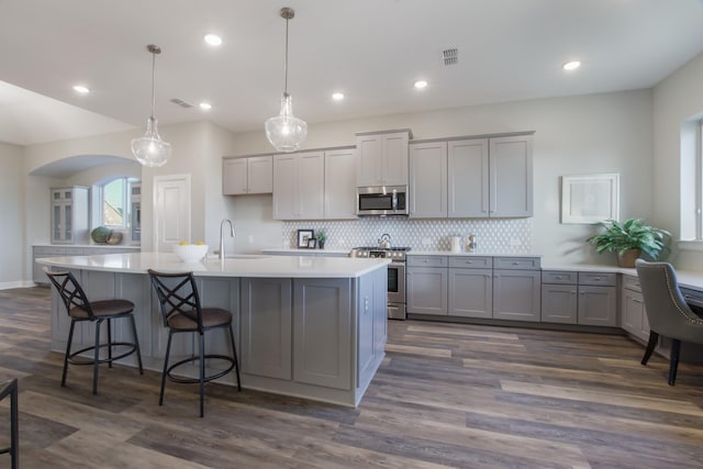 kitchen featuring gray cabinets, appliances with stainless steel finishes, decorative light fixtures, sink, and a kitchen island with sink