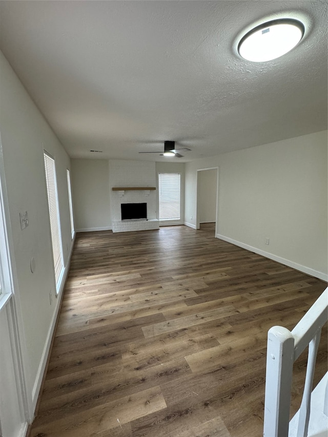 unfurnished living room with dark hardwood / wood-style flooring, a textured ceiling, ceiling fan, and a brick fireplace