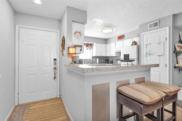 kitchen with light hardwood / wood-style floors, white refrigerator, white cabinets, kitchen peninsula, and a kitchen breakfast bar