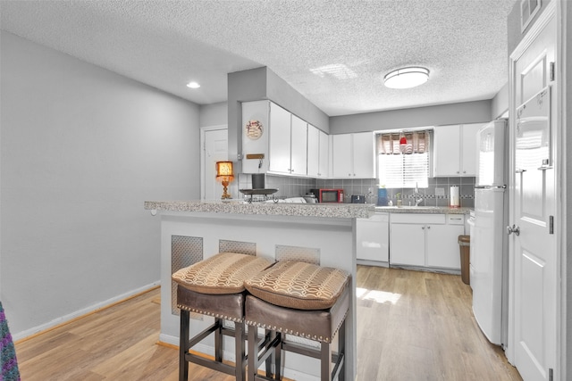 kitchen featuring light hardwood / wood-style floors, kitchen peninsula, sink, white fridge, and white cabinetry