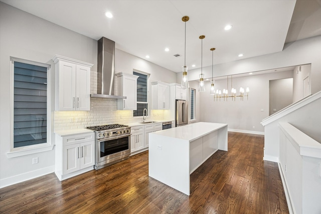 kitchen with a center island, sink, high quality appliances, wall chimney range hood, and decorative light fixtures